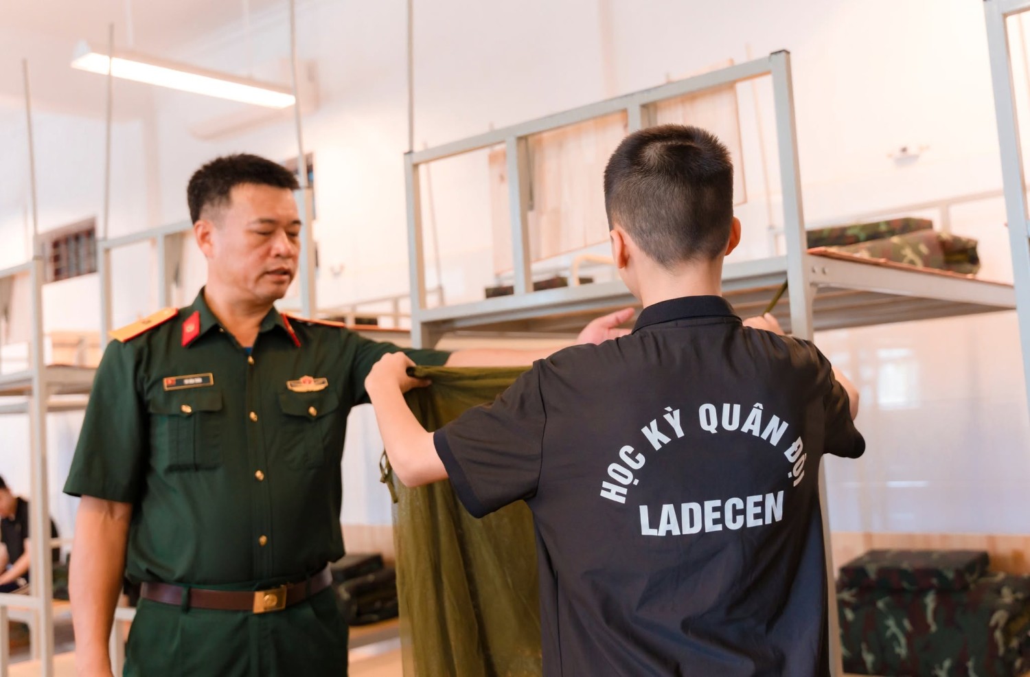 Người hướng dẫn hỗ trợ học sinh thực hành gấp chăn trong không gian nội trú